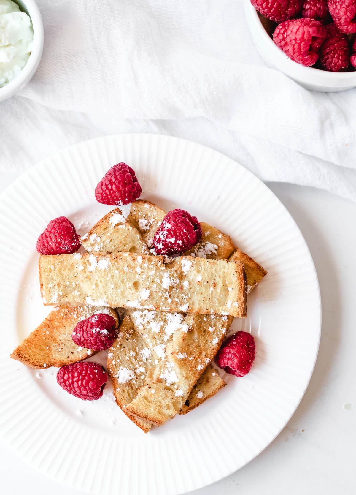 overhead of French toast sticks layered on top of one another topped with powdered sugar and fresh raspberries