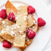 vegan french toast sticks on white plate topped with powdered sugar and fresh raspberries