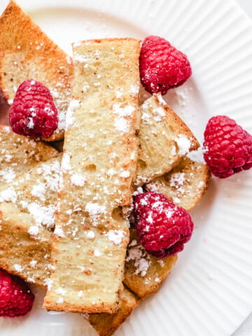 vegan french toast sticks on white plate topped with powdered sugar and fresh raspberries