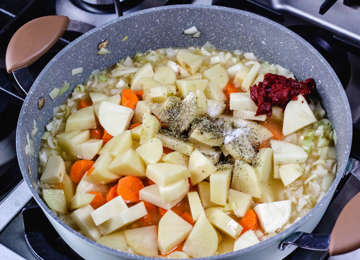 Carrots, potatoes, spices, and tomato paste in pot of onions and vegetable stock.