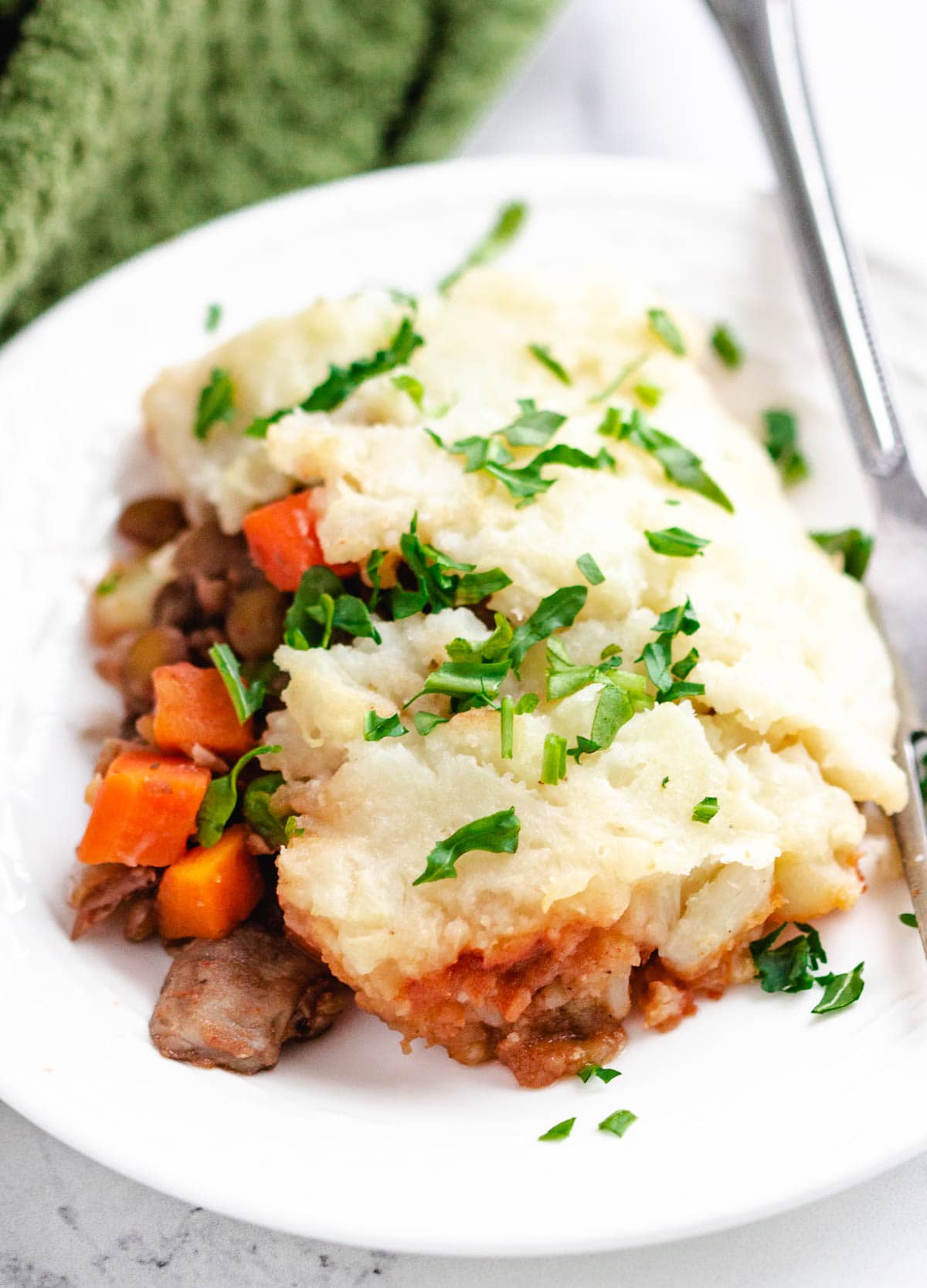 Serving of vegan lentil shepherd's pie on white plate topped with fresh herbs.