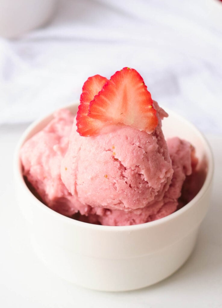 close up of vegan strawberry ice cream topped with fresh strawberry slices in white bowl