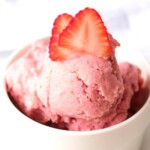 close up of vegan strawberry ice cream topped with fresh strawberry slices in white bowl
