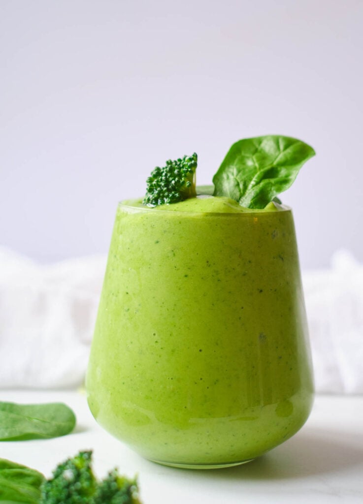 green smoothie in stemless wine glass topped with broccoli floret, and spinach leaves