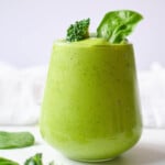 broccoli smoothie in glass topped with broccoli floret and spinach leaves