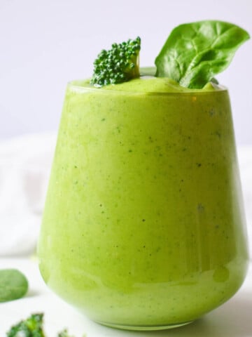 broccoli smoothie in glass topped with broccoli floret and spinach leaves