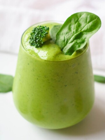 green broccoli smoothie in stemless wine glass garnished with broccoli floret and spinach leaf