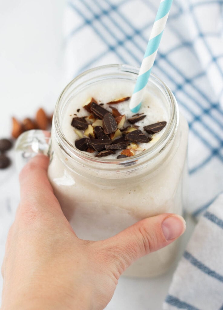 hand holding mug of vegan milkshake with chocolate and almonds on top