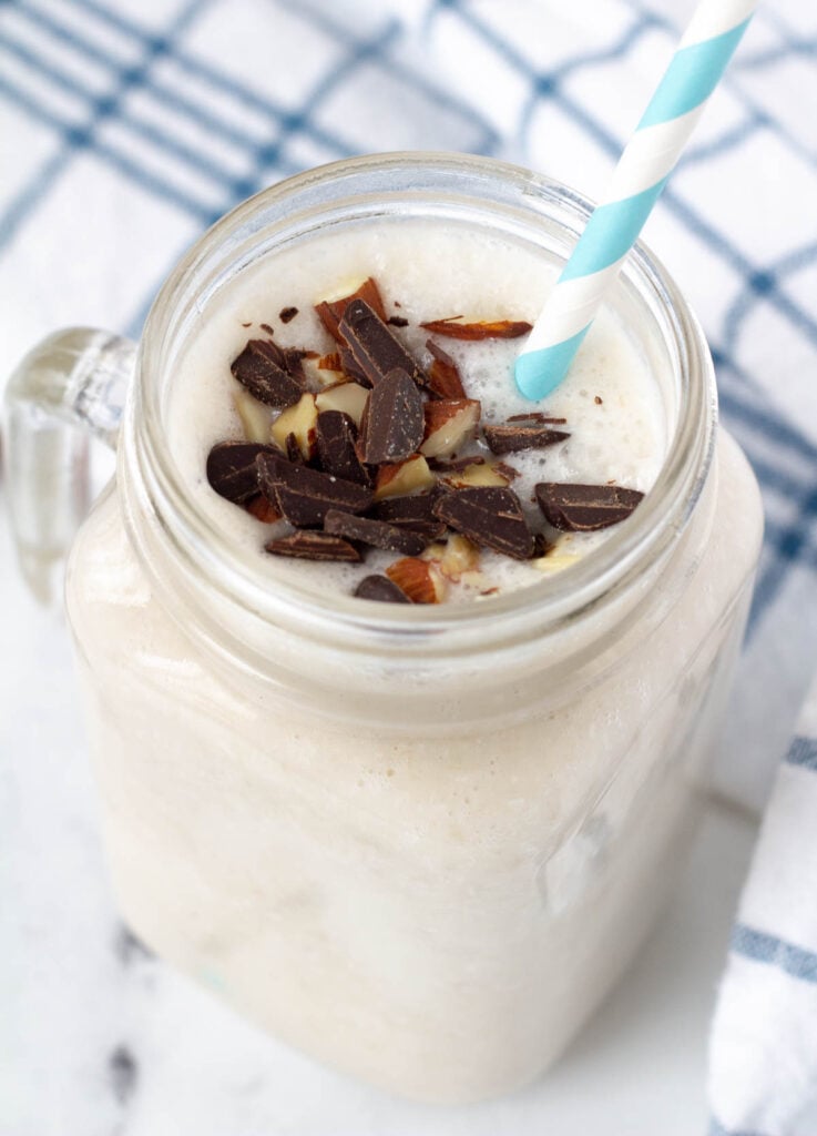 coconut milkshake in glass mug, with blue striped straw and topped with chocolate shavings and almonds