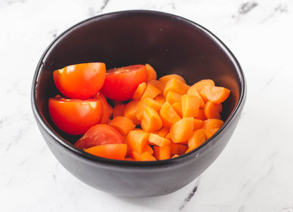 sliced tomatoes and diced carrots in small black bowl