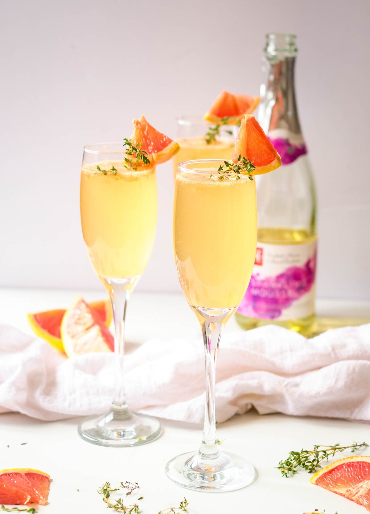 Grapefruit mimosas in champagne flutes garnished with fresh thyme and wedge of grapefruit.