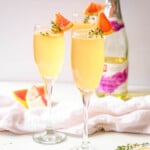 grapefruit mimosas in champagne flutes with thyme and grapefruit wedge