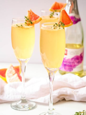 grapefruit mimosas in champagne flutes with thyme and grapefruit wedge