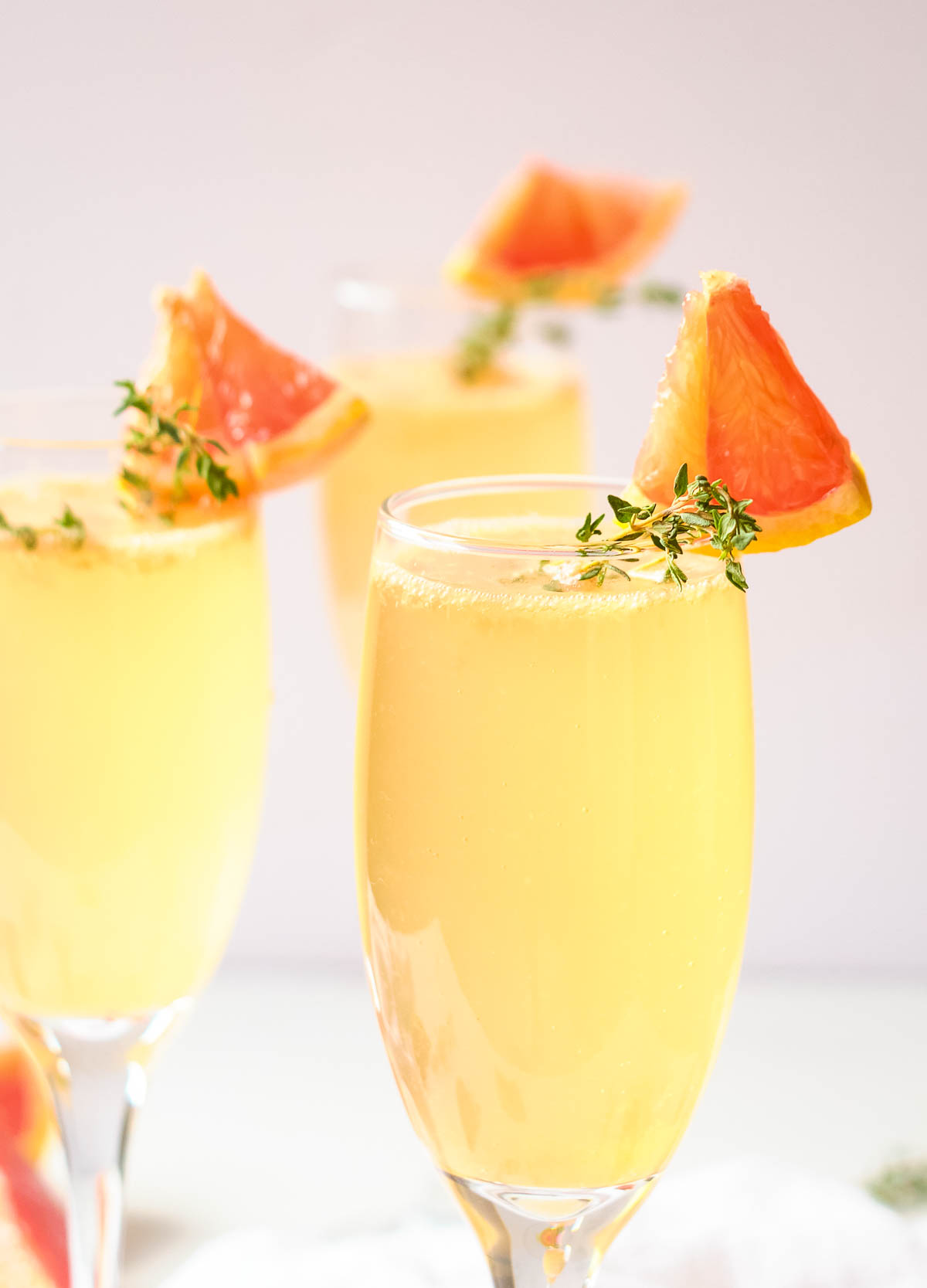 Easter mimosas in champagne flutes garnished with fresh thyme and wedge of grapefruit.