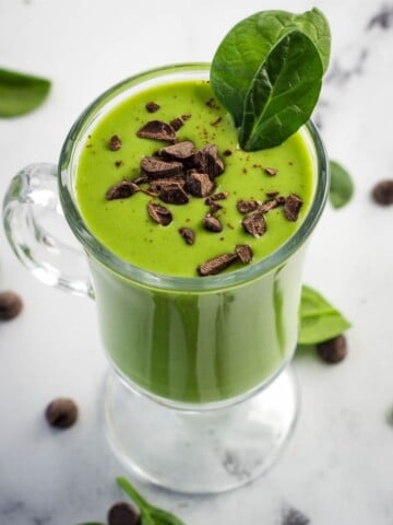 healthy vegan shamrock shake topped with chocolate shavings and spinach leaves