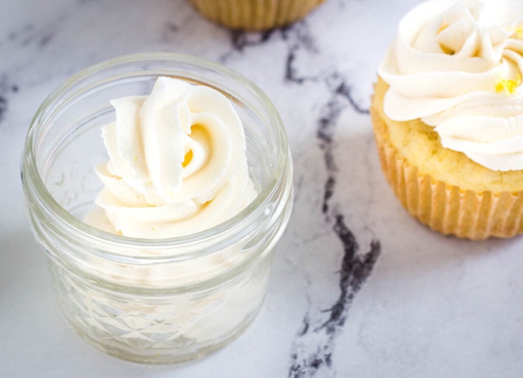 vegan buttercream frosting in glass jar next to cupcake