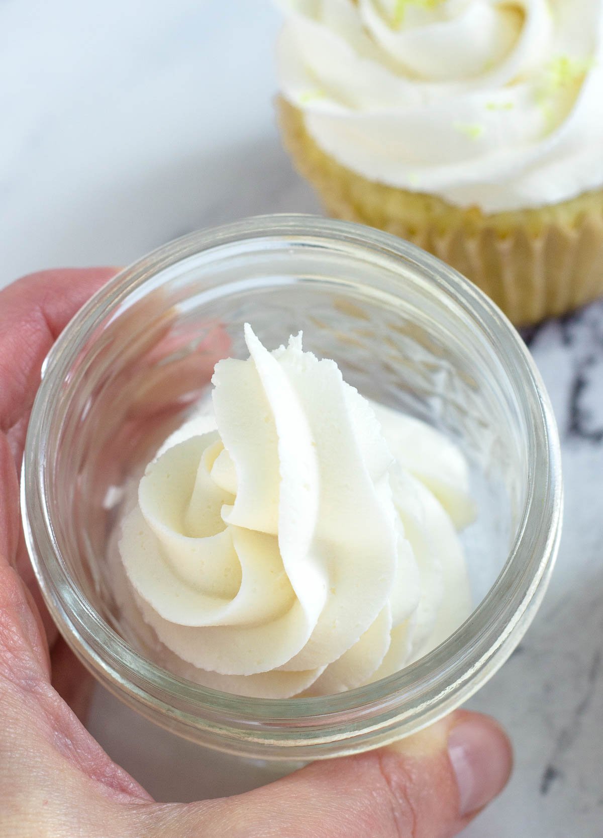 vegan buttercream frosting in glass jar with cupcake in the background