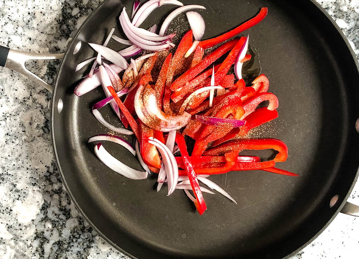 Pan with sliced red pepper, and red onions, topped with spices.