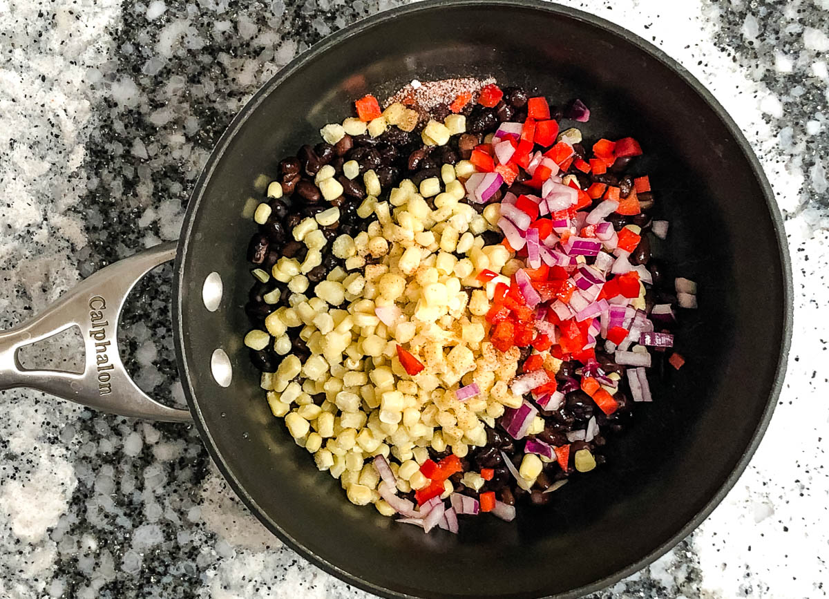 Pot with black beans, corn, red onion, red pepper, and spices.