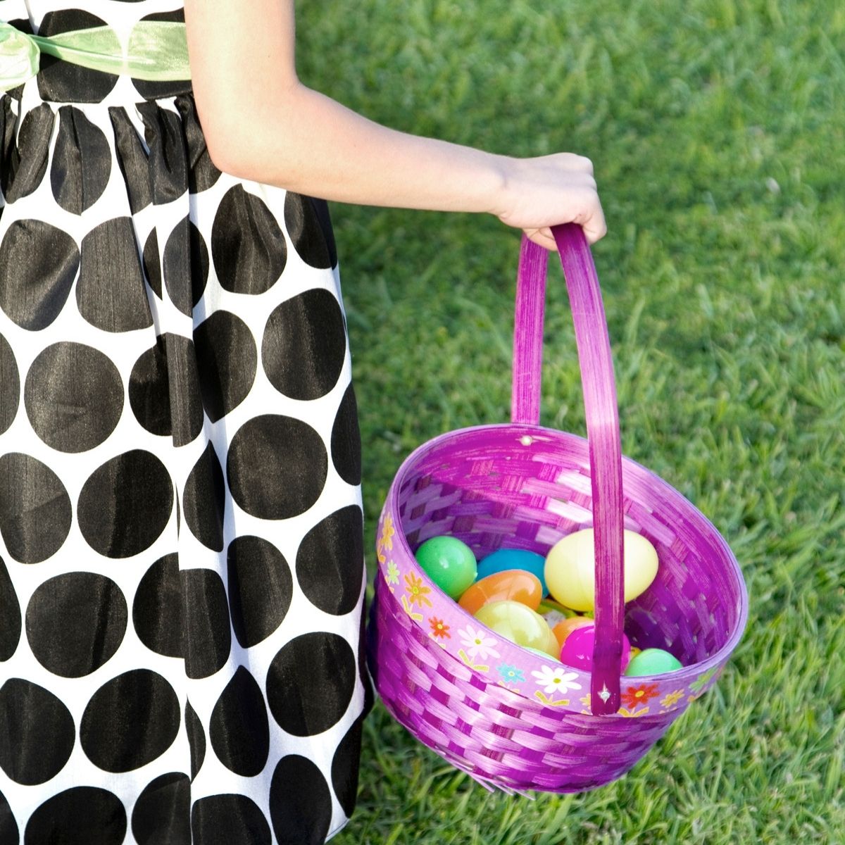 little girl in polka dot dress holding purple Easter basket filled with plastic eggs
