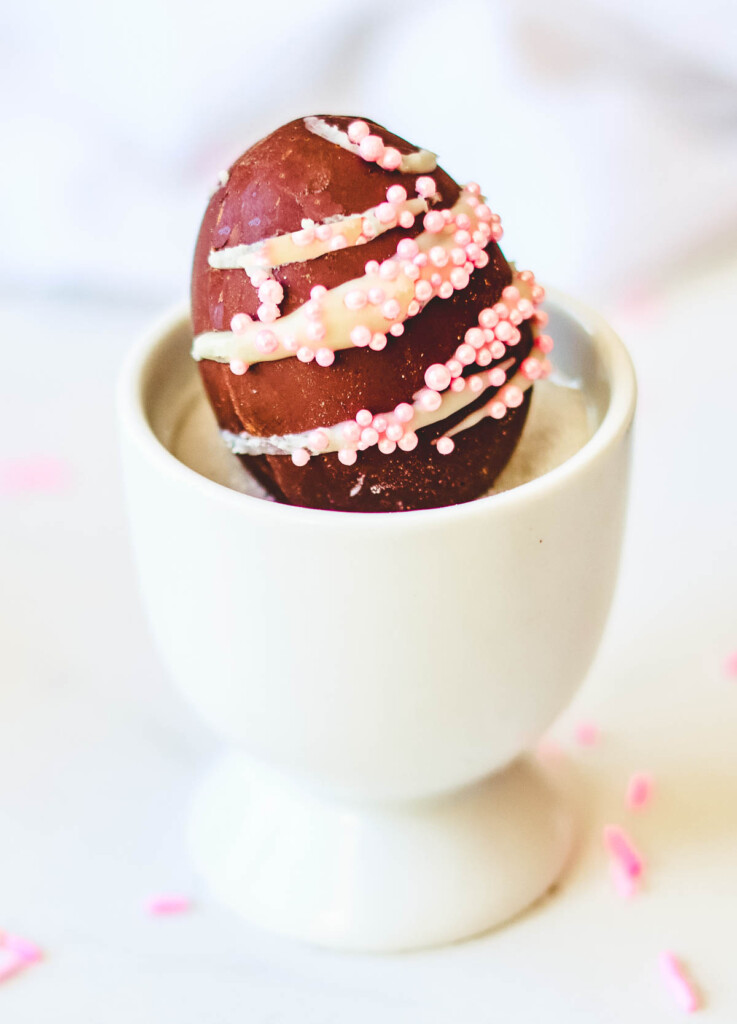 chocolate vegan easter egg with white frosting drizzle and pink sprinkles