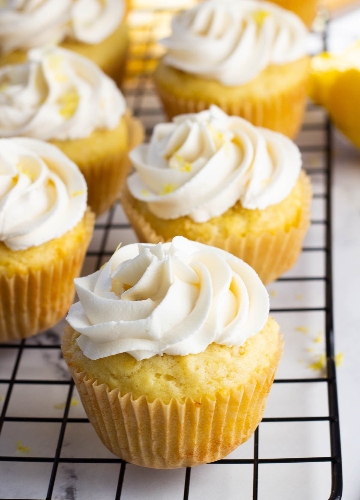 Vegan lemon cupcakes on cooling rack, topped with buttercream frosting and lemon zest.