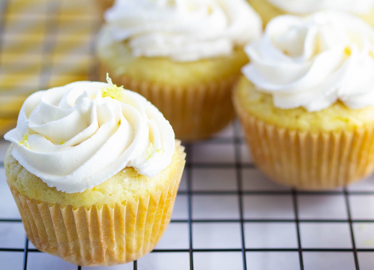 Vegan lemon cupcakes with buttercream frosting and lemon zest on cooling rack.