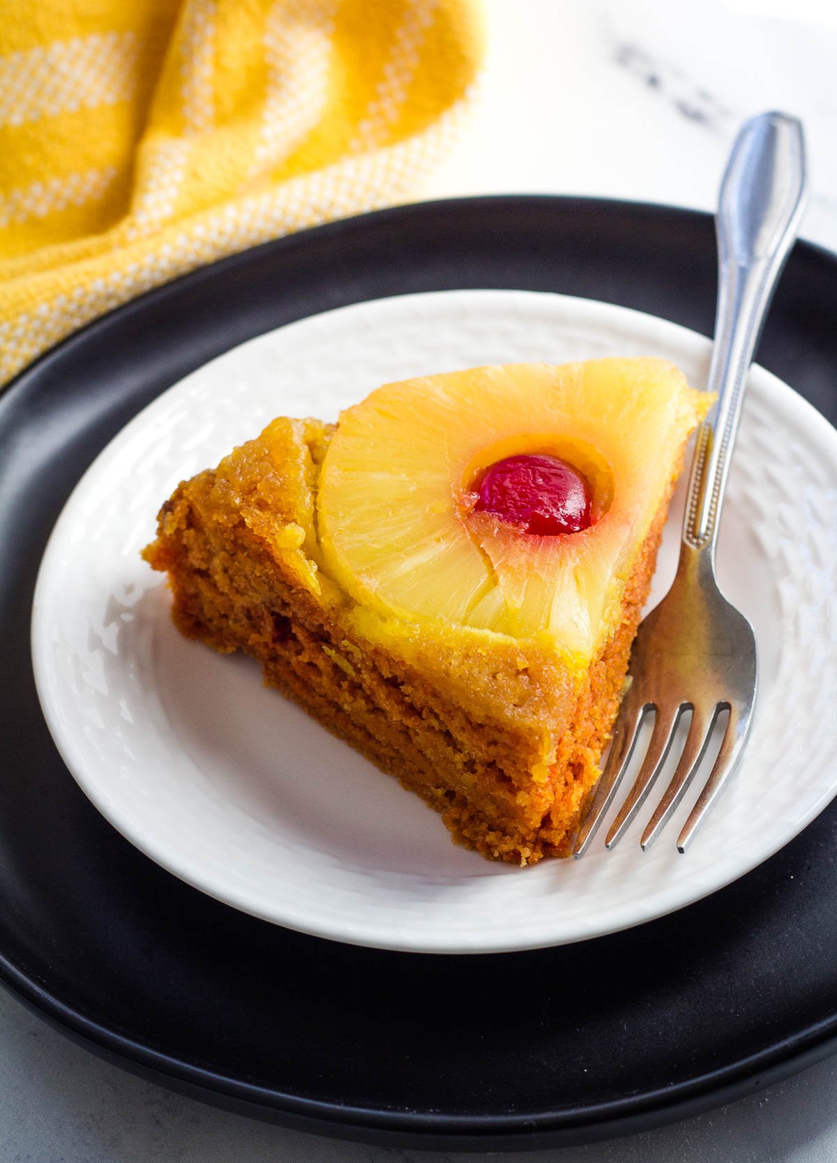 slice of vegan pineapple upside down cake on white and black plate with fork