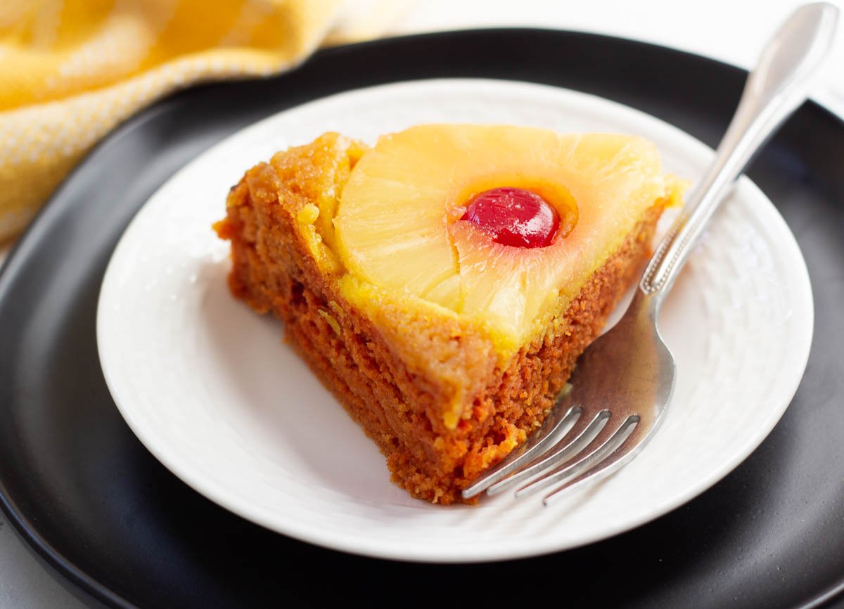 Vegan pineapple upside down cake slice on white plate with fork.