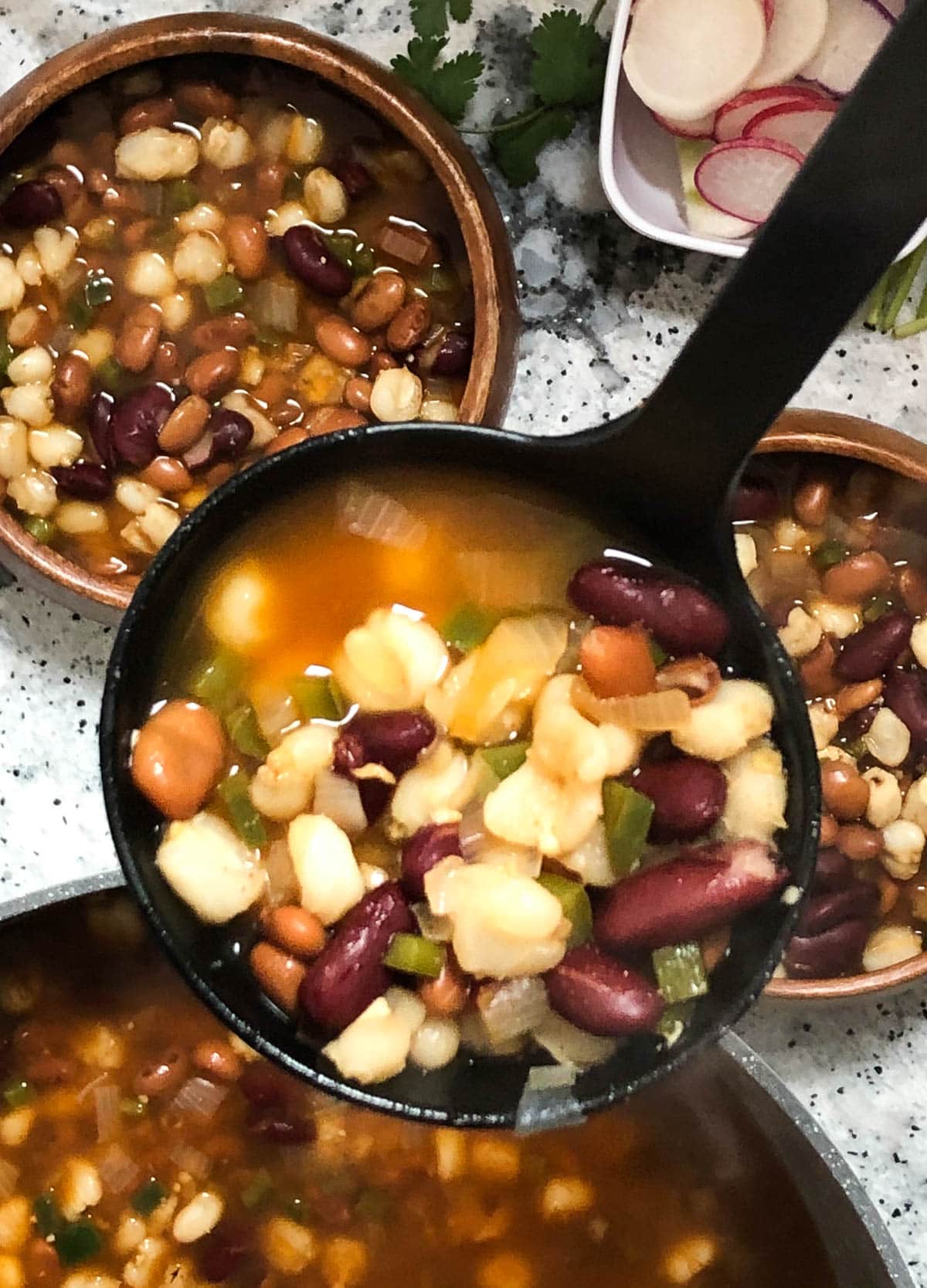 bean and hominy soup scooped into ladle for serving