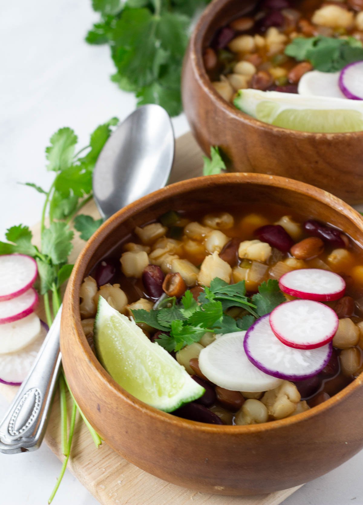Vegan pozole in wood bowl topped with radishes, cilantro, and lime wedge.