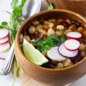 vegan pozole in wood bowl topped with radish slices, cilantro and lime wedge