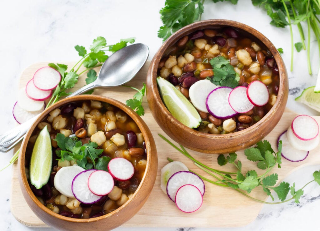 vegan pozole in two wood bowls topped with radishes, cilantro, and lime wedge