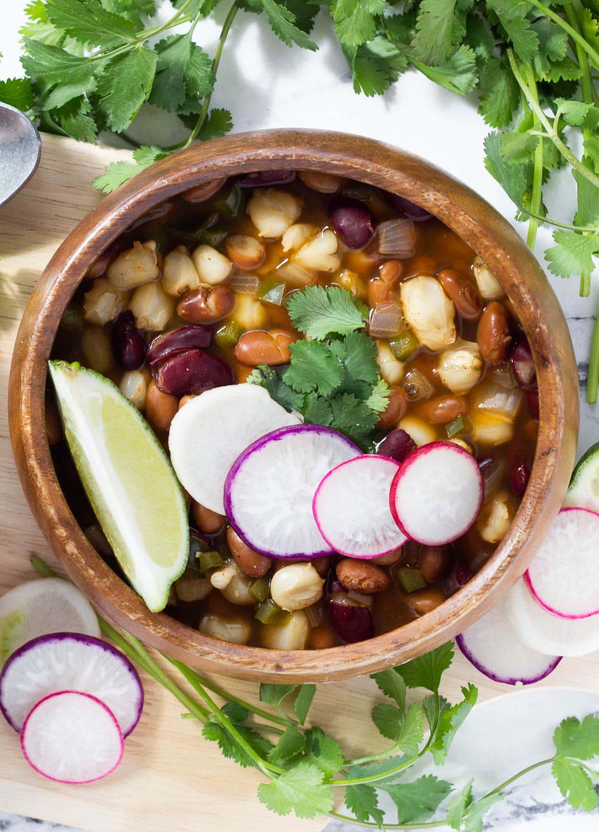 vegan pozole in wood bowl topped with radish slices, cilantro, and lime wedge