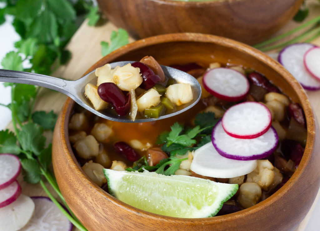 vegan pozole in wood bowl with spoon scooping a bite