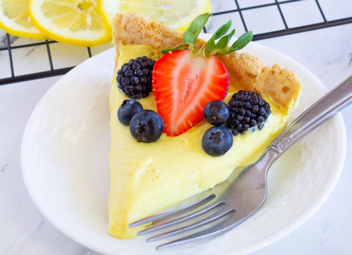 Slice of vegan lemon tart topped with strawberry, blackberries, and blueberries.