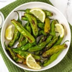 air fryer shishito peppers in white bowl with lemon wedges