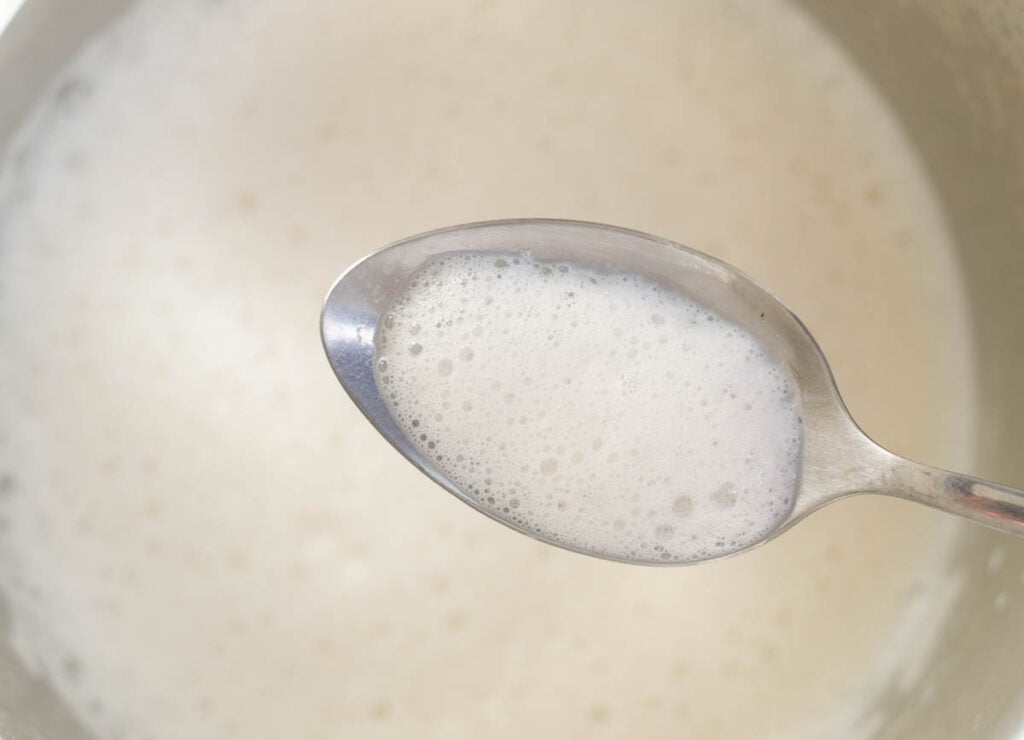spoon scooping foam out of pot filled with foamy almond milk
