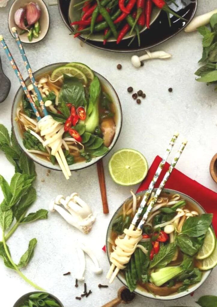 vegan pho in two bowls with noodles wrapped around chop sticks