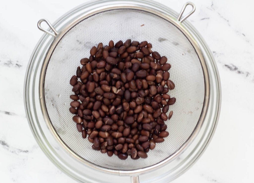 black beans in metal strainer over glass bowl