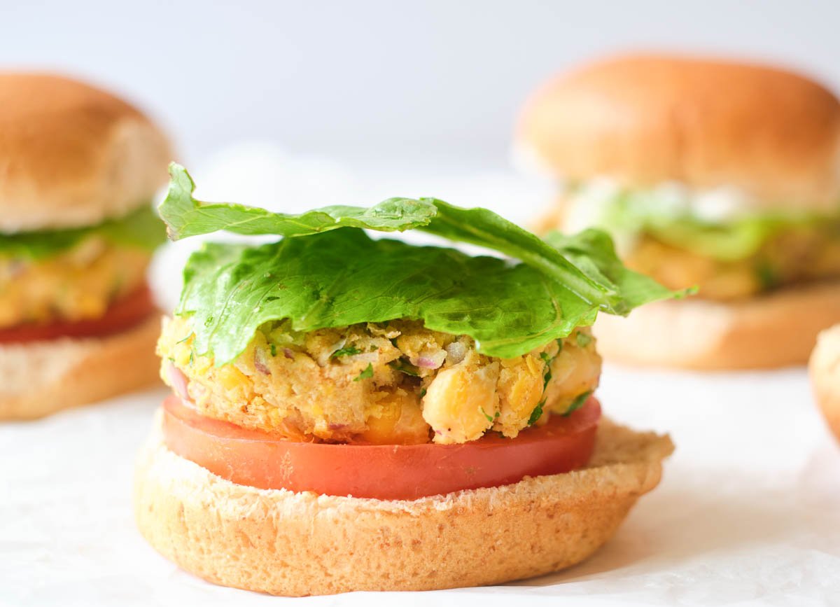Bottom of whole wheat bun topped with tomato slice, chickpea burger, and two pieces of lettuce.