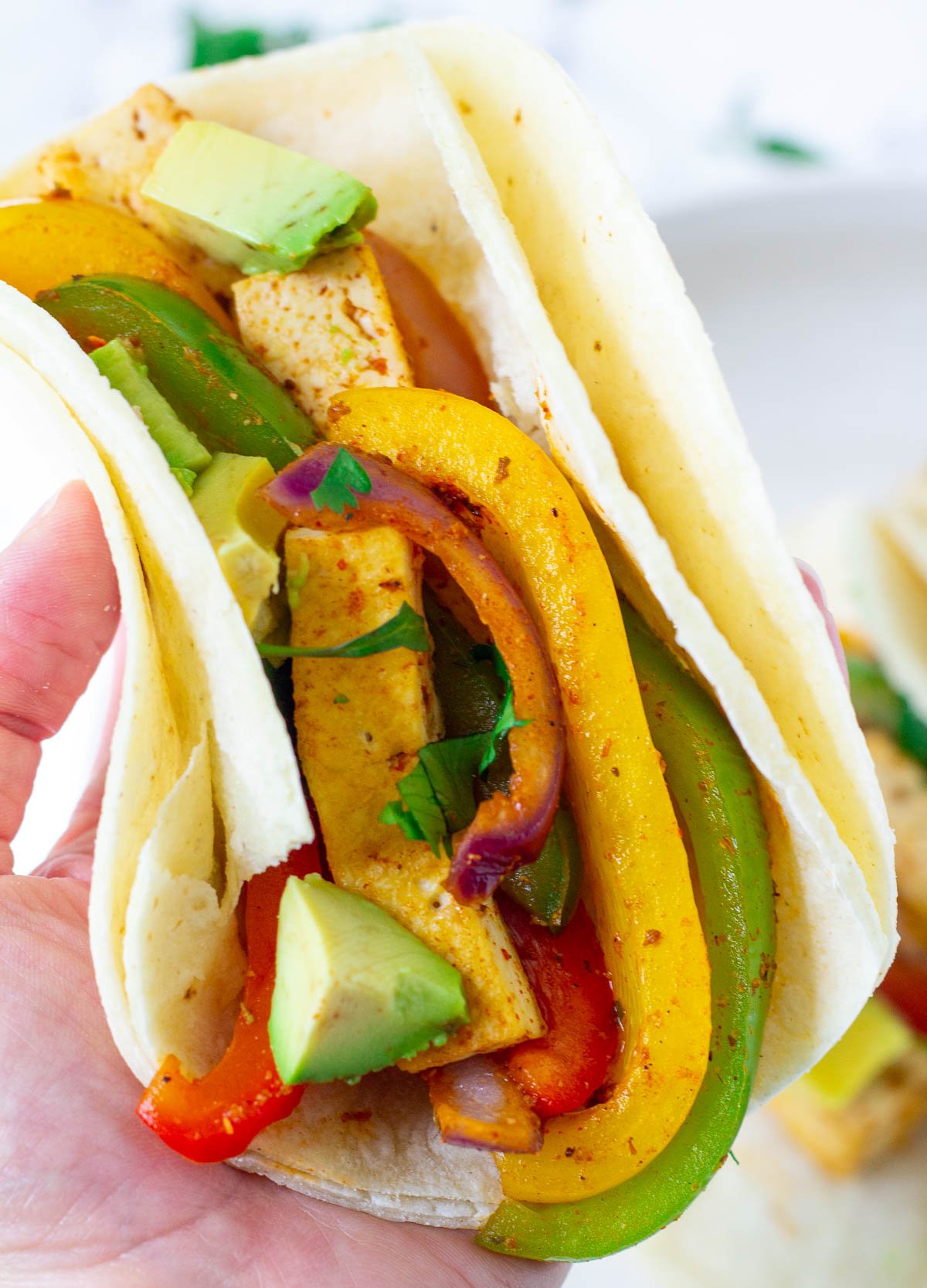 Hand holding a fajitas in a corn tortilla with tofu and peppers.