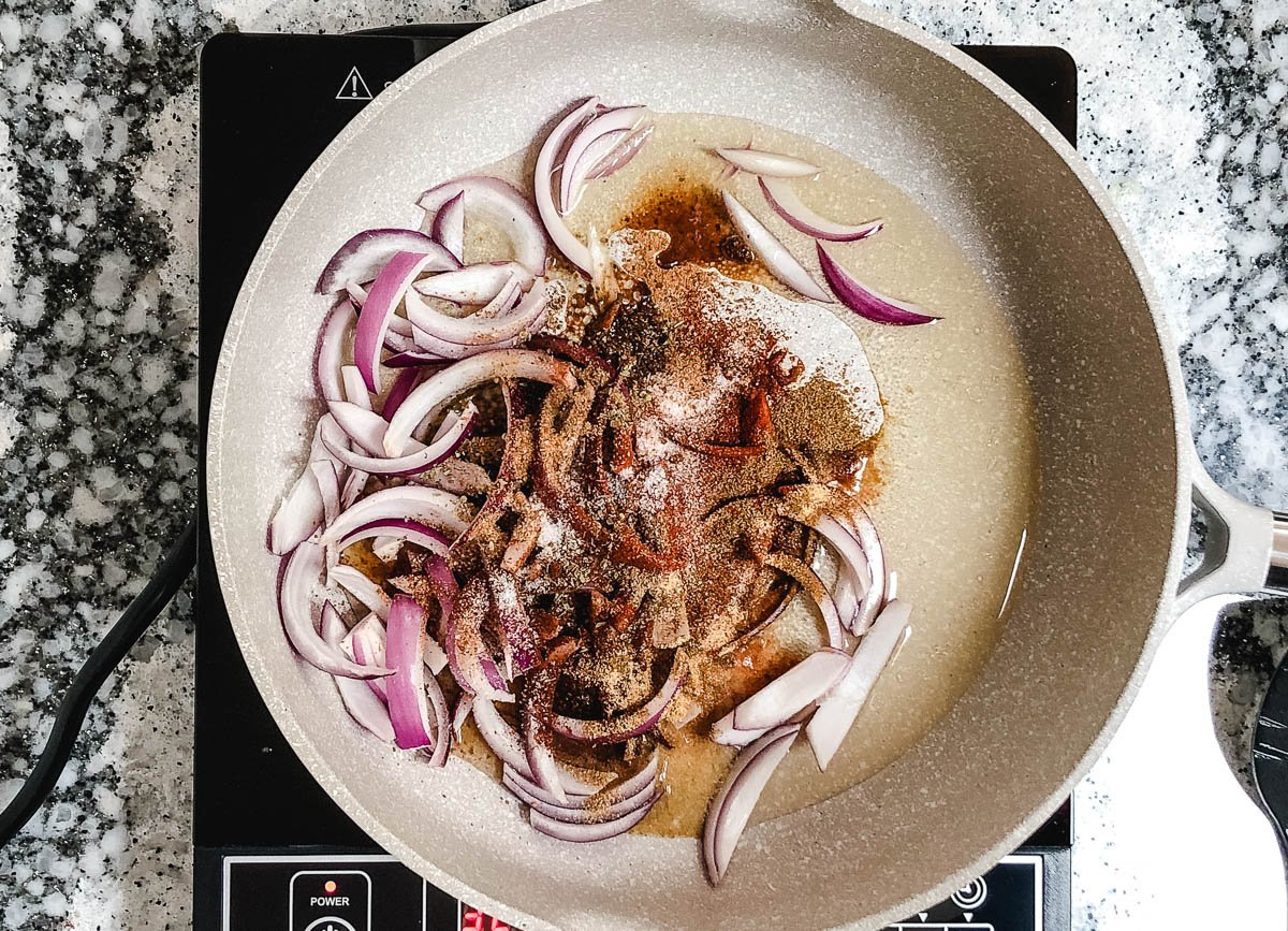 Large skillet with red onion slices and spices.
