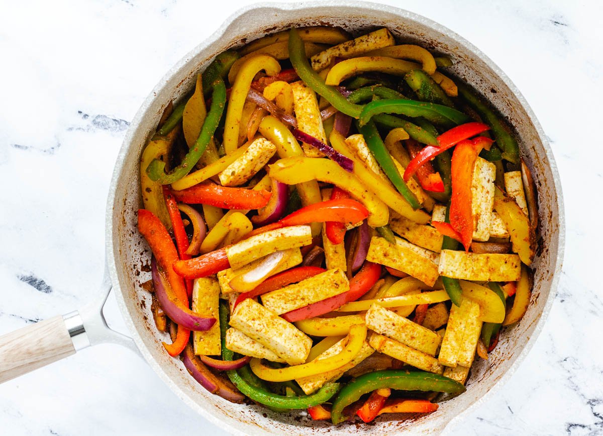 Large skillet filled with tofu chunks and peppers with seasoning.