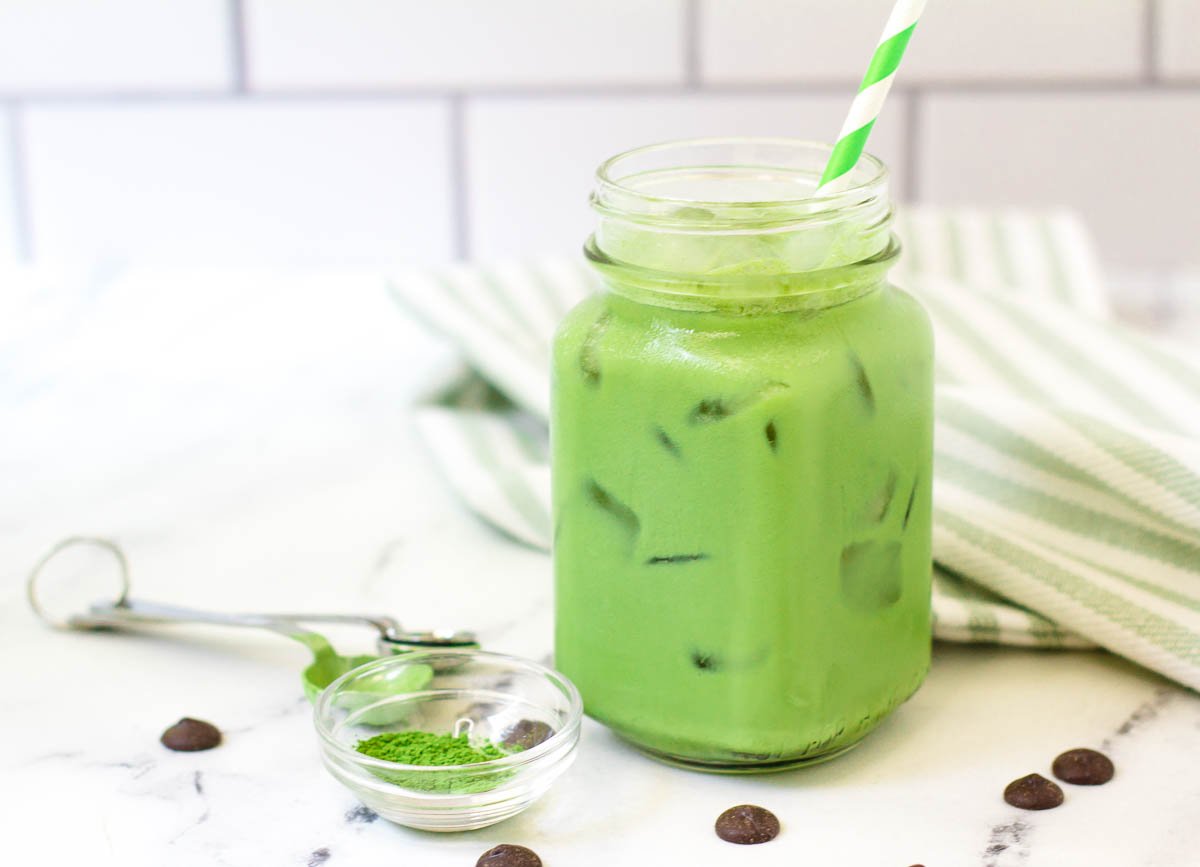 iced matcha latte in glass mug served over ice with a sprinkle of chocolate chips and matcha powder on counter