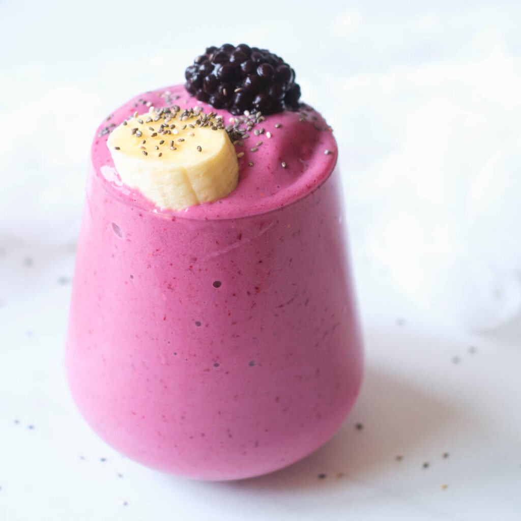 strawberry blackberry banana smoothie in glass topped with banana slice, blackberry and chia seeds