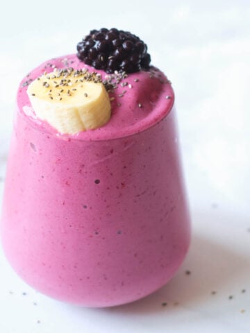 strawberry blackberry banana smoothie in glass topped with banana slice, blackberry and chia seeds