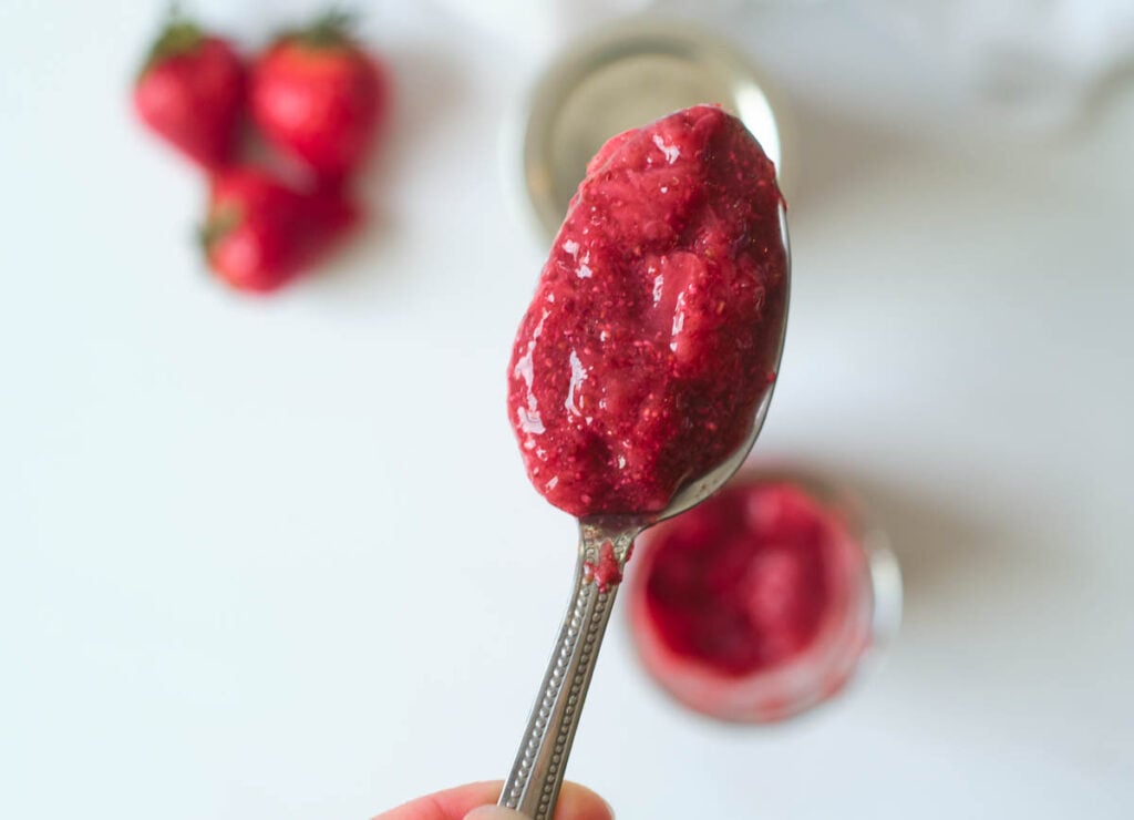 Healthy strawberry chia jam on spoon held over mason jar.