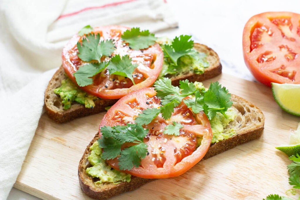 tomato and cilantro on top of avocado toast, served on cutting board