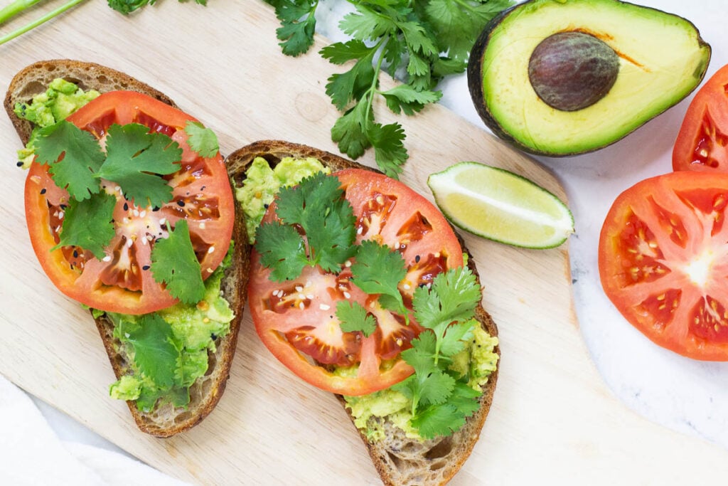 avocado toast topped with tomato slices and cilantro served on cutting board with a wedge of lime